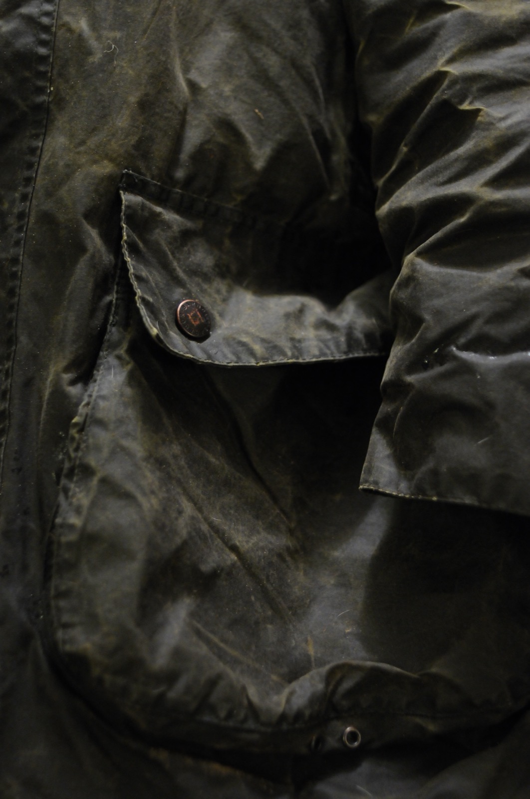 A well-worn olive Barbour waxed jacket with flap pocket